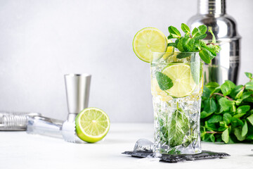 Mojito summer alcoholic cocktail drink with lime, white rum, soda, cane sugar, mint, and ice in highball glass on gray background.  Steel bar tools. Copy space