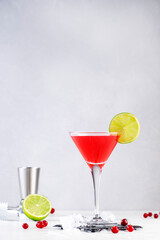 Ccosmopolitan alcoholic cocktail drink with vodka, liqueur, cranberry juice, lime and ice. Gray table background, bar tools, copy space