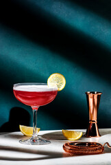 Pink lady classic cocktail drink with dry gin, grenadine syrup, lemon juice and egg white, dark green background, bright hard light, shadow pattern