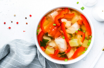 Fish soup with paprika, potatoes, tomatoes and parsley in ceramic soup bowl on white table background, top view