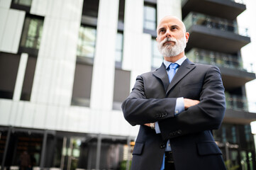 Mature bald stylish business man portrait with a white beard outdoor with folded arms