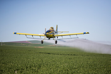 Close up image of crop duster airplane spraying grain crops on a field on a farm - obrazy, fototapety, plakaty
