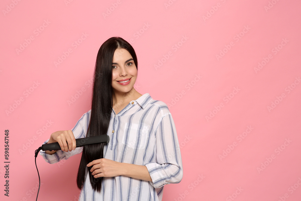 Poster Beautiful happy woman using hair iron on pink background. Space for text