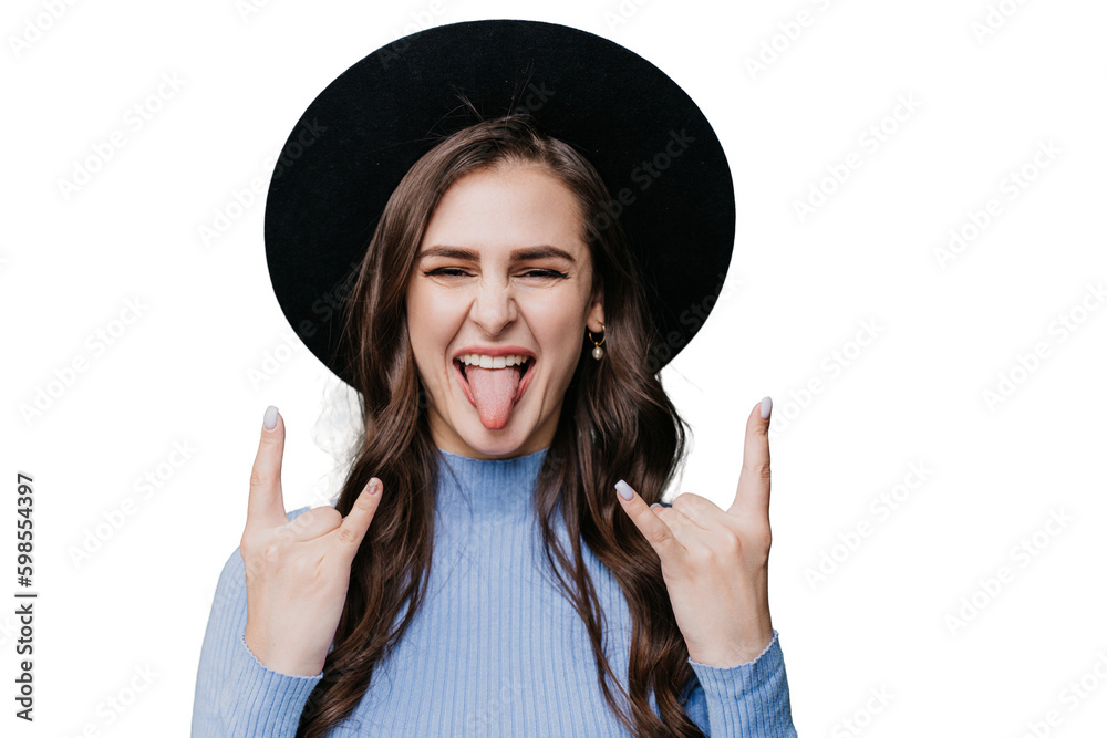 Wall mural Playful brunette female hipster in hat with brim and lilac sweater shows tongue and rock n roll gesture by both hands over transparent background. Crazy girl having fun, excited woman. Youth.