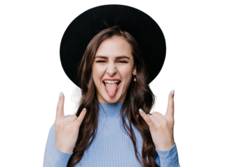 Playful brunette female hipster in hat with brim and lilac sweater shows tongue and rock n roll gesture by both hands over transparent background. Crazy girl having fun, excited woman. Youth.