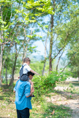 Naklejka premium happy family in the park. father piggyback walk with his son in a green park. kid dream outside concept. father and son are walking on green grass. happy family daddy carries fun son around his neck