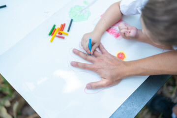 Family activity drawing son using crayons to draw father's hand