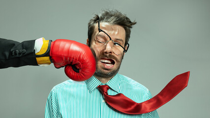 Mature man, businessman in red tie getting boxing punch in jaw from business competitors over grey background. Concept financial loses, business fall, deadlines, economic crisis - obrazy, fototapety, plakaty