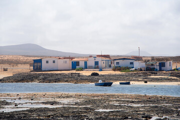 Fototapeta na wymiar View of Majanicho village in the touristic Fuerteventura, with small houses in front of a turquoise sea with two fishing boats on a clear day in the Canary Islands.
