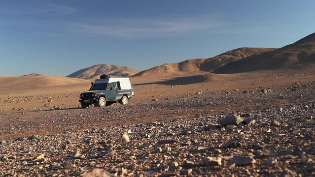 four wheel drive off road vehicle parked in between the dry and arid sand dunes of the secluded atacama desert in chile at sunset.