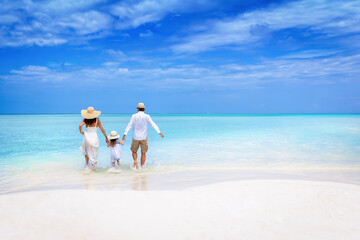 A happy family runs into the turquoise ocean of a  tropical paradise beach in the Maldives during their vacation time