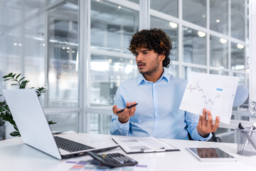 Upset financier showing online report, man working inside office nervously showing document,...