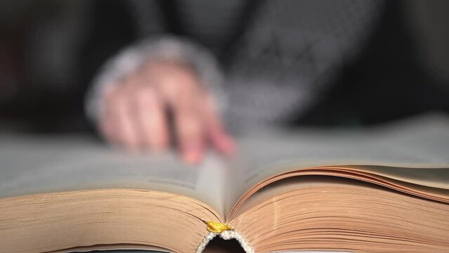 Stock VHand turning pages of a book. Slow motion. Person's hand reading a book and holding fingers along the lines. Cinematic light at home or library. Concept for reading, studying, reseaideo Project