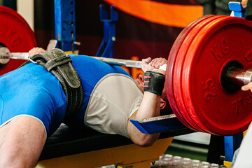 athlete powerlifter ibench press powerlifting competition, barbell with three red plates of 25 kg...