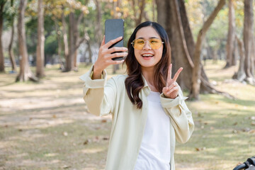 Happy woman riding bicycle and taking selfie at park.