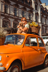 A young beautiful woman in sunglasses stands in a retro convertible car with her puppy