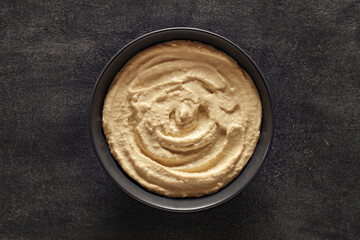 Hummus in grey bowl, on dark background, top view, space to copy text
