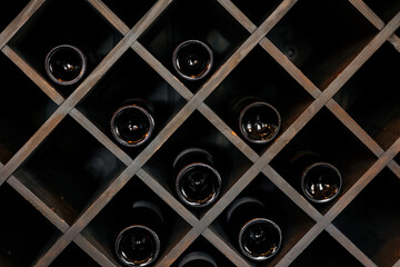 Elite dark glass wine bottles stacked on wooden racks in cellar, market, restaurant or home....