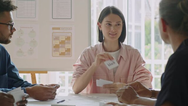Young female teacher showing word cards with English words and explaining them to adult migrant students during lesson in language school