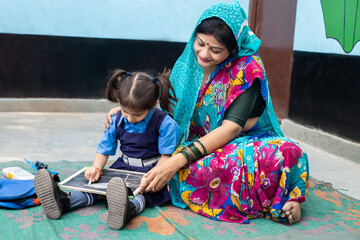 Young indian teacher help little girl student with writing on slate board while sitting on floor. Kid wearing school uniform studying at government school. - obrazy, fototapety, plakaty