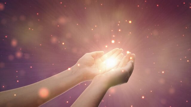 Conceptual Visualization Of Male Or Female Hands Reaching Out In Prayer On Magical Dark Purple Background. Person Connecting With Higher Spiritual Energy Through Bright Light In Their Palms.