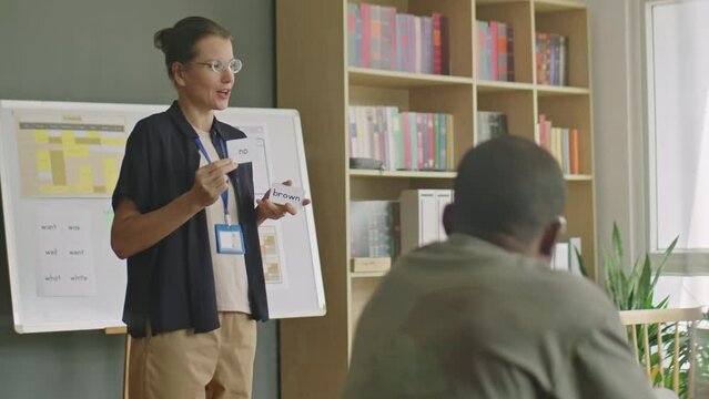 Female english teacher showing cards with new words and talking to group of immigrant students during lesson in language school