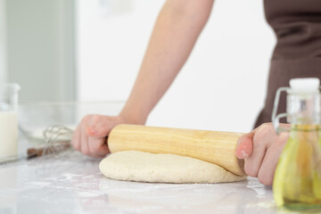 Obraz na płótnie Canvas Pizza dough with ingredients on white table. Woman hands keep rolling pin with flour in white bright kitchen, baking background, menu, recipe. Preparing bread dough in kitchen at home.