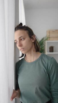 Sad young woman looking through window. Depression and mental health concept.