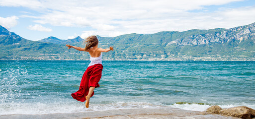 Woman in red dress jumping at the lake