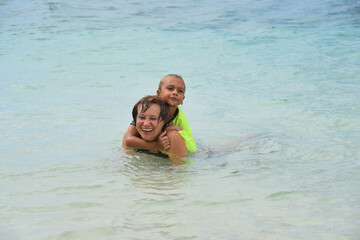 Happy grandson and grandmother 50-60 age having fun and laughing in the water on the beach. Senior woman with child. Concept - travel, vacation, happy family, retirement, active elderly people.