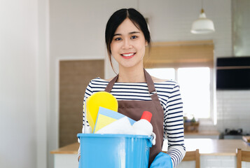 Unrecognizable millennial maid holding bucket with cleaning supplies indoors, closeup of hands. Cropped view of housewife with detergents, ready for house cleanup. Sanitary service concept