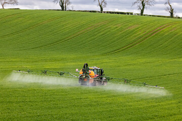 Crop Spraying in large field with trees on skyline