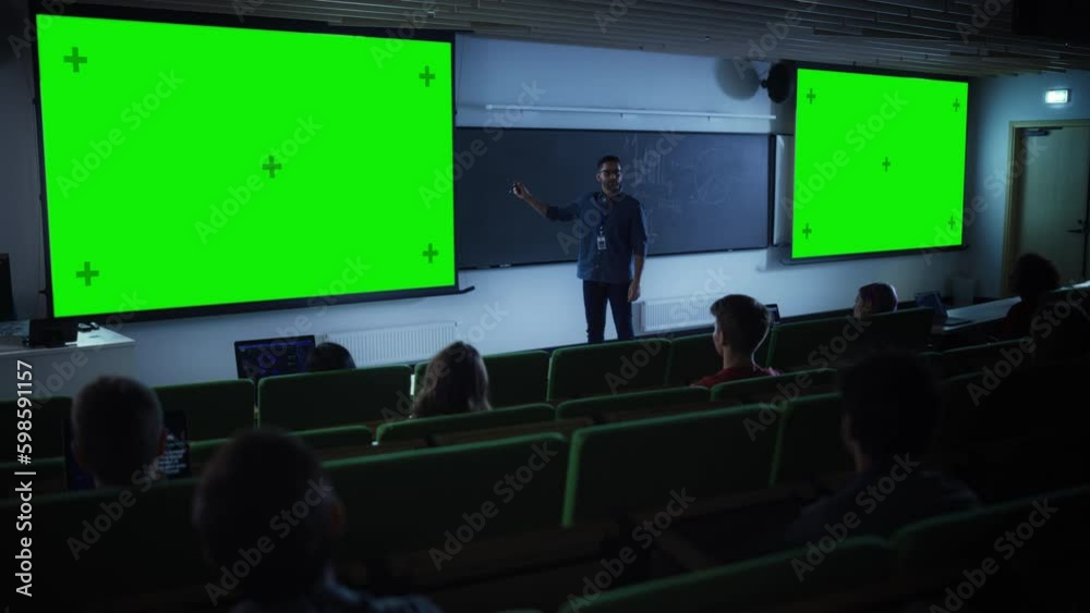 Aufkleber Young Male Teacher Giving a Lecture, Showing Slides on a Green Screen Mock Up Display to a Diverse Multiethnic Group of Female and Male Students in Dark College Auditorium
