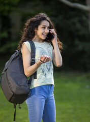 Pretty teenage girl with school bag talking on phone in park