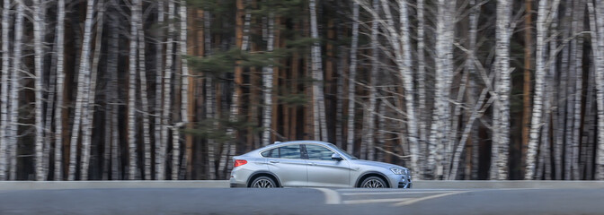 Car drives along a country road next to a forest.