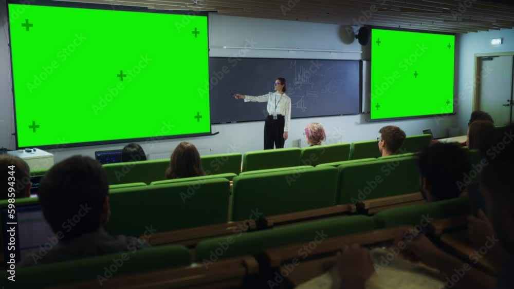 Poster Young University Professor Giving a Lecture, Pointing on a Green Screen Mock Up Display. Group of Talented Diverse Students Study in Modern Classroom. Female Teacher Showing Content on Big Screens