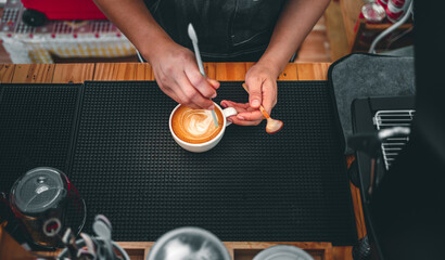 Close-up of the hand of a barista with a wooden spoon making or preparing coffee foam in a cup of coffee.barista making coffee