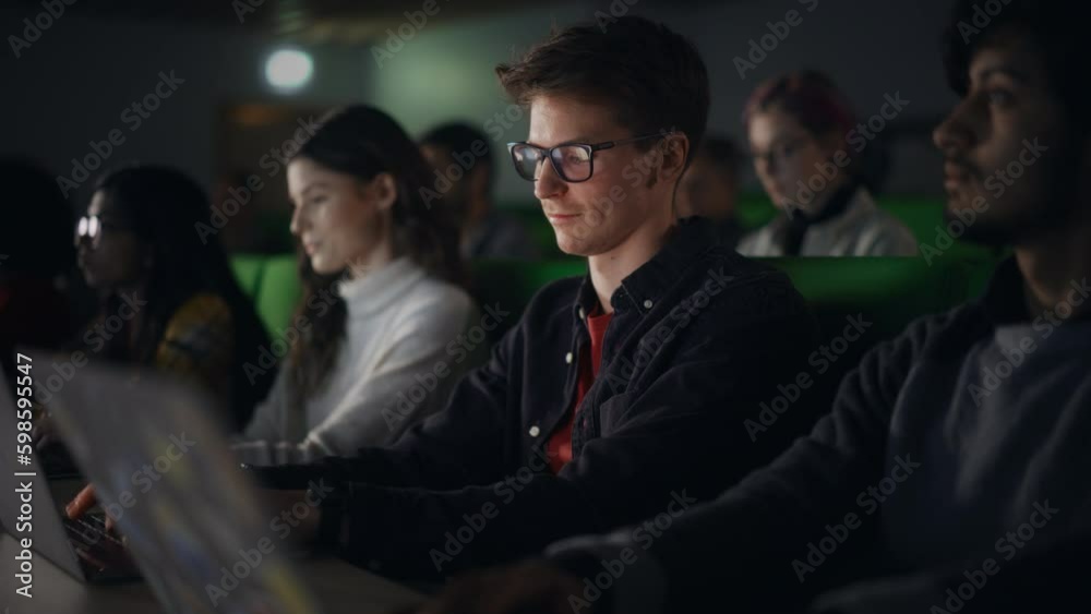 Poster Young Male Student Studying in University with Diverse Multiethnic Classmates. He is in Uplifting Mood and is Using a Laptop Computer. Patiently Listening to Professor's Lecture and Taking Notes