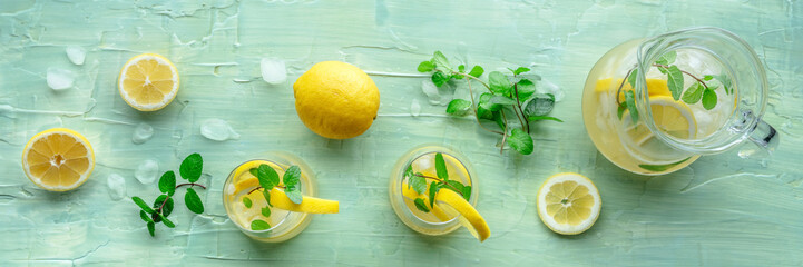 Lemonade with mint panorama. Lemon water drink with ice. Two glasses and a pitcher on a blue background, overhead flat lay shot. Detox beverage. Fresh homemade cocktail © laplateresca