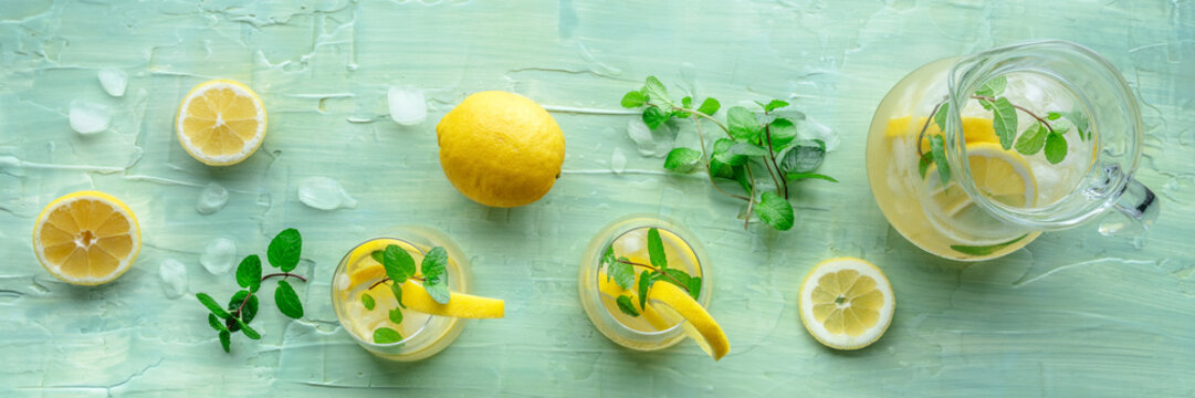 Lemonade with mint panorama. Lemon water drink with ice. Two glasses and a pitcher on a blue background, overhead flat lay shot. Detox beverage. Fresh homemade cocktail