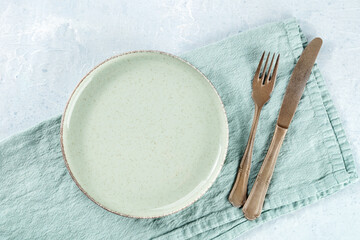 An empty green plate, with a fork and a knife, overhead flat lay shot on a slate background, with a teal napkin, the concept of dinner