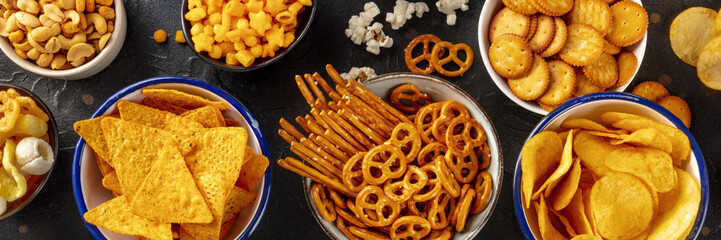 Salty snacks, party mix panorama. An assortment of crispy appetizers, overhead flat lay shot on a...