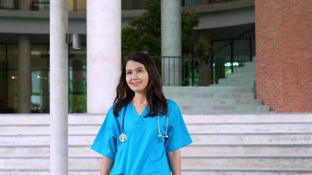 Portrait of a confident, happy, and smiling Asian medical woman doctor or nurse wearing blue scrubs uniform.