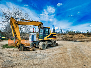 Yellow excavator on an earthen construction site in an industrial zone