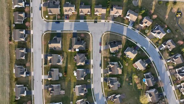 American neighborhood overhead view. Sprawling cookie cutter development during golden hour with shadows. Aerial top down establishing shot. Cinematic reverse shot.