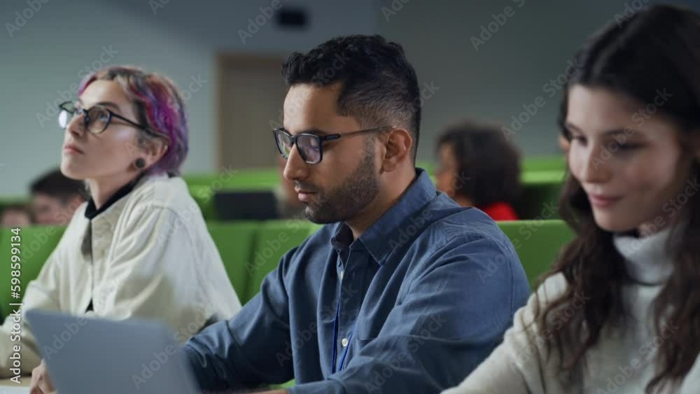 Poster Young Handsome Male Student Studying in University with Diverse Multiethnic Classmates. Young Man is Writing Down Lecture Summary in Notebook to Prepare for College Exams