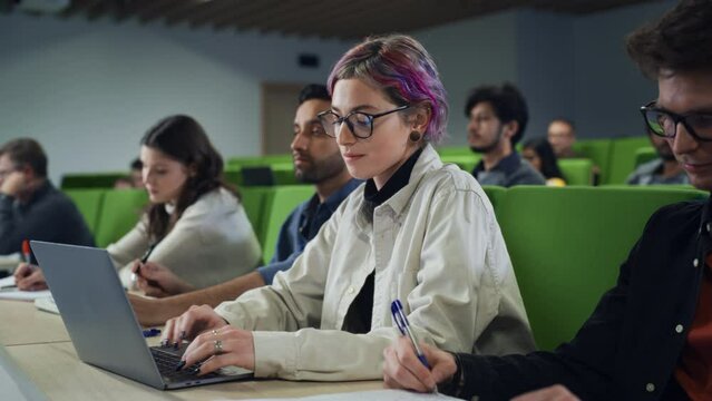 Smart Creative Female Student Studying in University with Diverse Multiethnic Classmates. Young Woman with Colored Short Hair is Using a Laptop Computer. Taking Notes from a Lecture in College