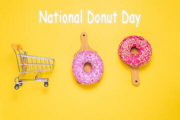 National Donut Day, pink donut with a shopping cart over the yellow background. Sweet, dessert,...