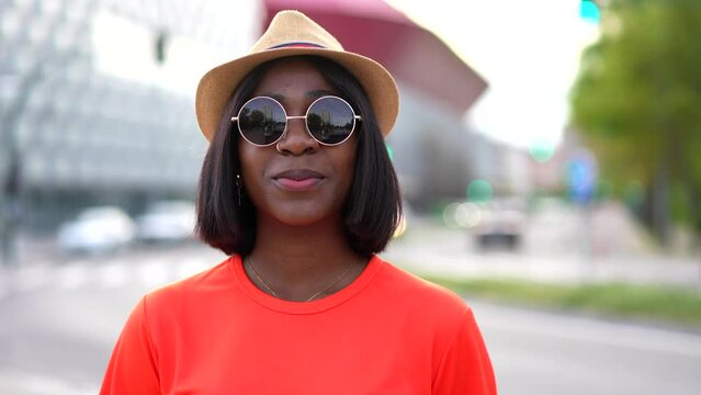 Young black woman in orange t-shirt, sunglasses, and hat, enjoying summer in the city, lifestyle photos