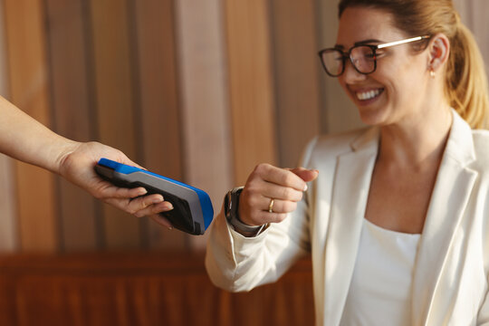 Contactless payment: Working woman paying with with her smartwatch on card reader in a coffee shop